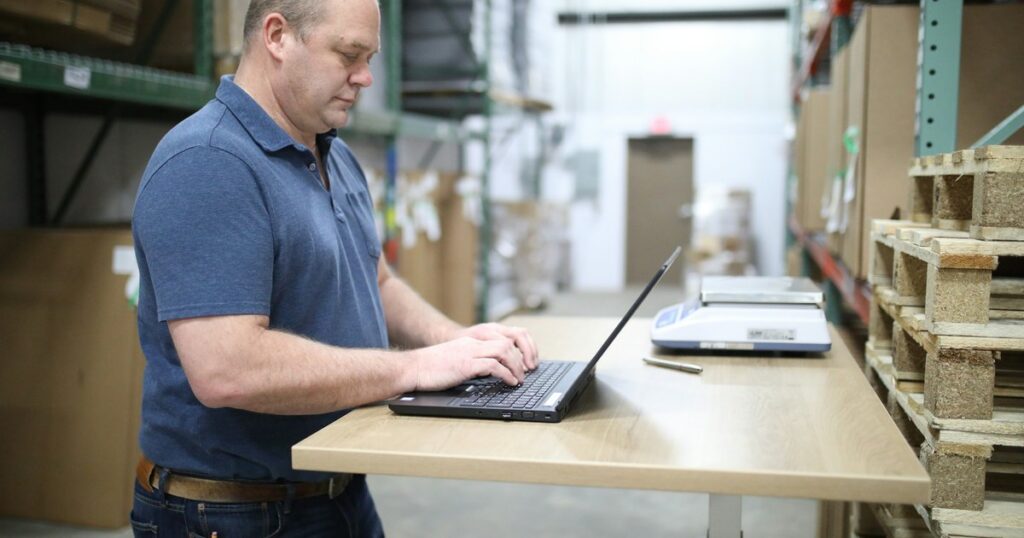 Logistics worker checking email on a laptop in a warehouse
